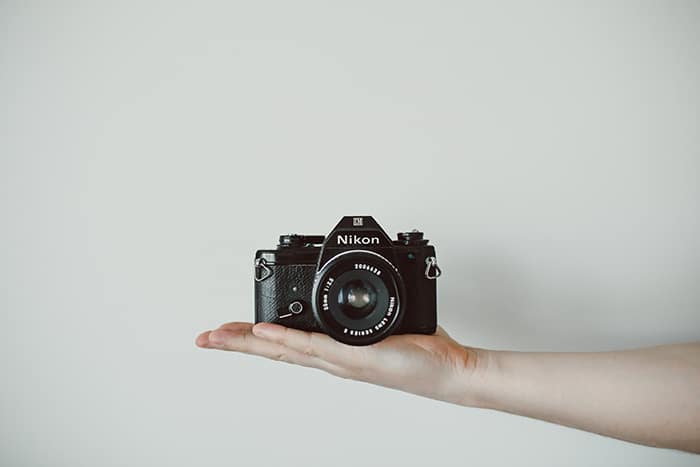 Una cámara Nikon balanceada sobre la mano extendida de una persona - asignaciones de fotografía