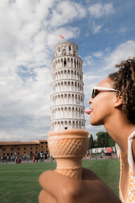 Divertida toma de fotografía en perspectiva forzada de una niña que posa para que parezca que está lamiendo la torre inclinada de Pisa en un cono de helado