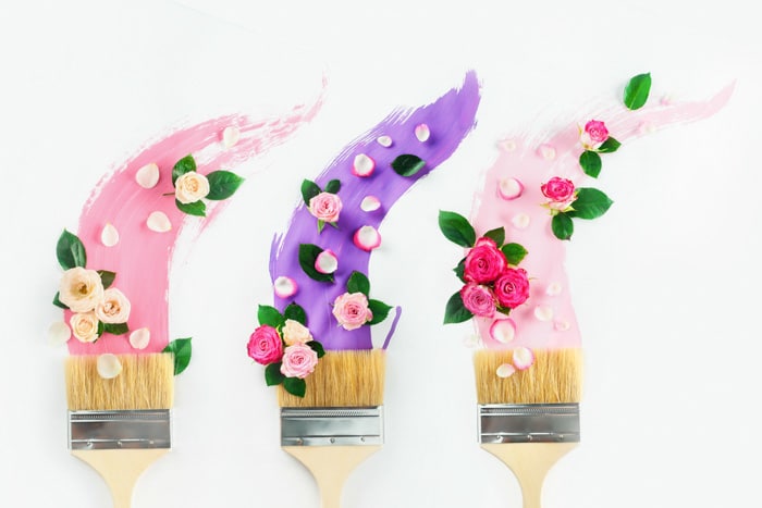 Pinceles con pinturas en tonos rosas y violetas, rosas y pétalos, sobre un fondo blanco.  Pintura de primavera plana creativa laical.  Concepto de decoración del hogar.