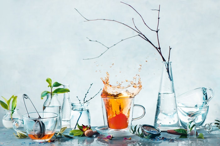 Taza de té con un toque dinámico y botellas de vidrio con plantas verdes y ramas de árboles en un bodegón primaveral de alto perfil.  Concepto de limpieza y frescura