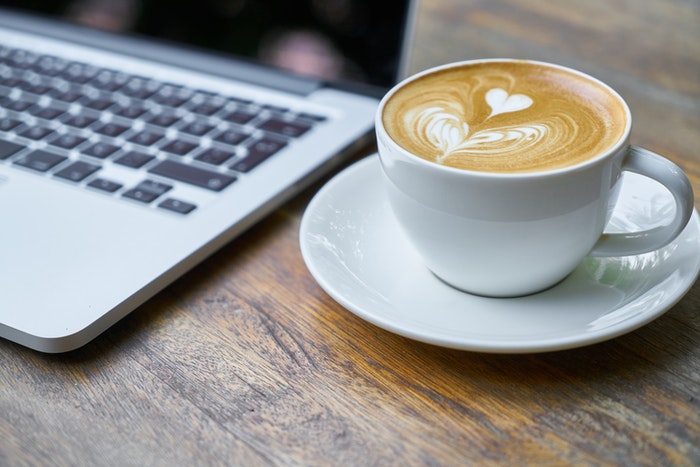 Una taza de café al lado de una computadora portátil.