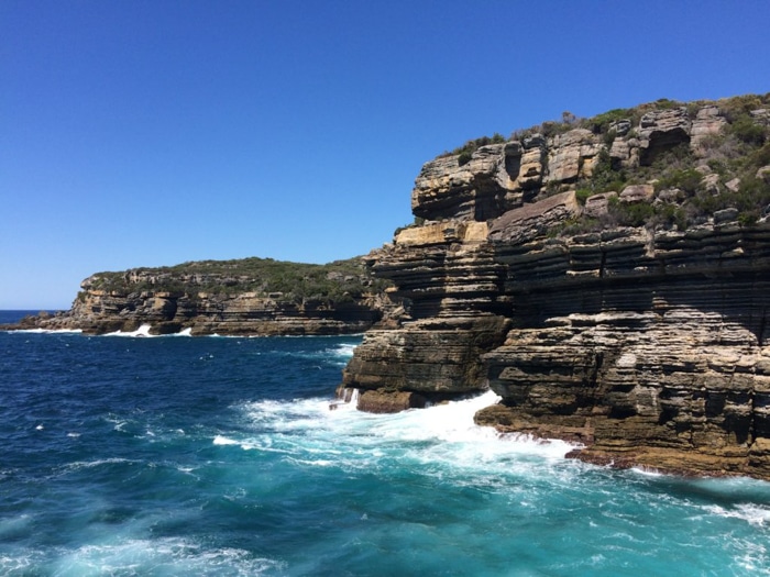 aguas turquesas y olas espumosas rompiendo contra un acantilado rocoso contra un cielo azul brillante - consejos de edición de fotos para fotografía de teléfonos inteligentes
