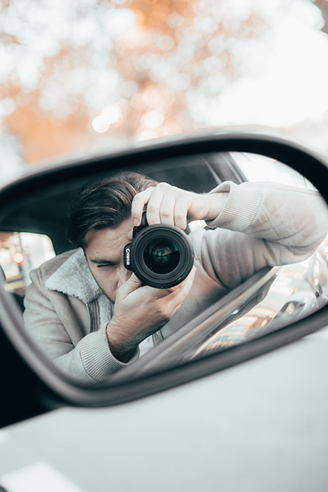 Reflexión en un retrovisor de coche que muestra a un hombre que sostiene una cámara