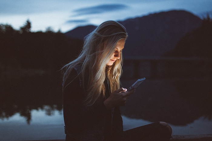 Un retrato de una mujer de cabello rubio con su teléfono inteligente al aire libre con poca luz