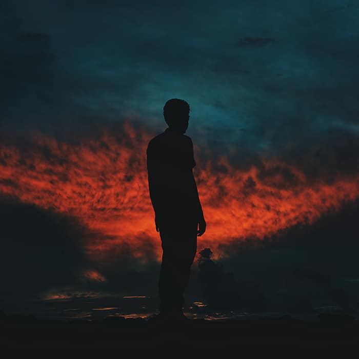 La silueta de un hombre contra un cielo ardiente por la noche - asignaciones de fotografía