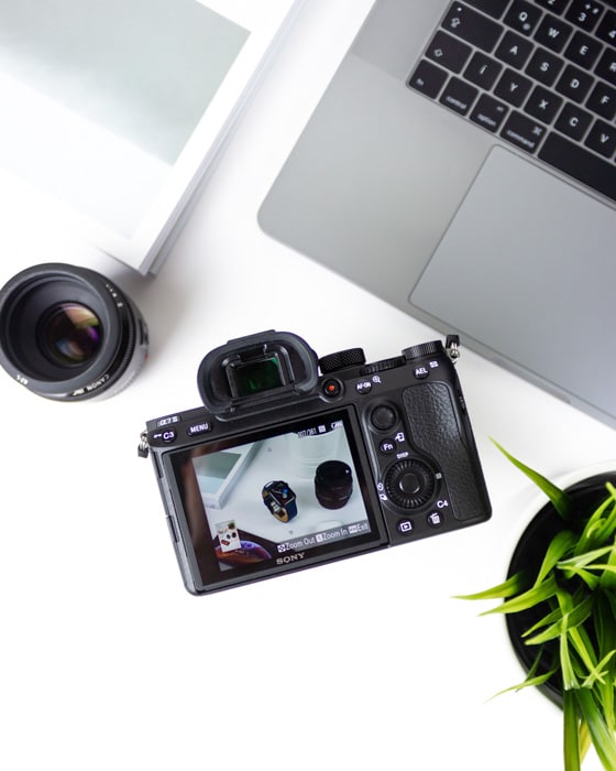 Una cámara digital, un objetivo, una computadora portátil y una planta sobre una mesa blanca: guía para diferentes tipos de archivos de fotos