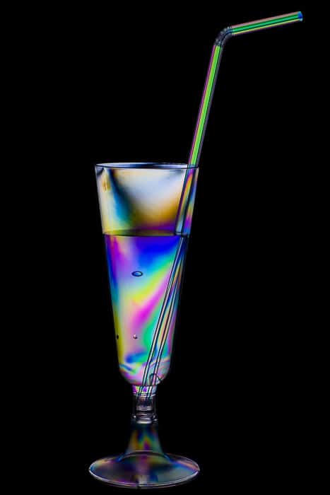 Efecto arcoiris en una copa de cóctel de plástico y pajita.
