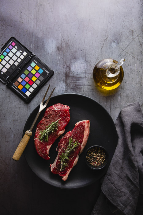 Bodegón de fotografía de alimentos que incluye un plato de carne cruda, aceite de oliva y corrector de color - equipo de fotografía comercial