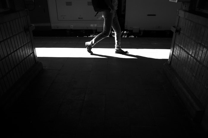 Imagen en blanco y negro que muestra las piernas de una persona caminando por un pasillo iluminado