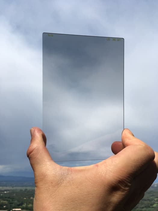 Cerrar foto de una mano sosteniendo un filtro de densidad neutra graduado hacia el cielo