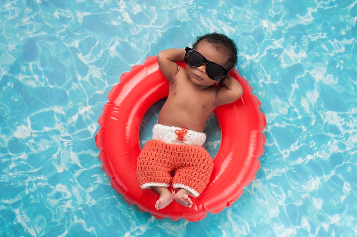 Idea divertida de la fotografía del recién nacido de un bebé posado en gafas de sol en un anillo de goma en una piscina