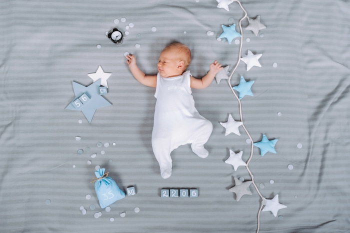 Idea de fotografía aérea del recién nacido del bebé descansando en una cama junto a accesorios y juguetes