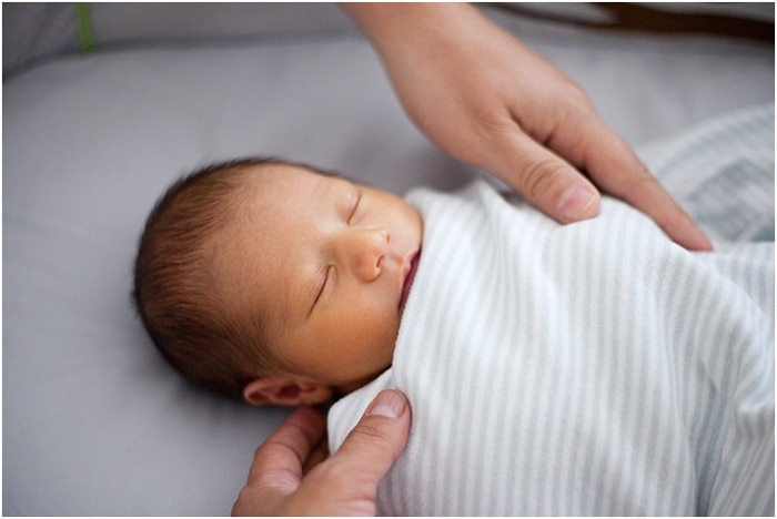 Cerca del bebé envuelto y durmiendo, con las manos de los padres sobre él durante una sesión de retrato de recién nacido