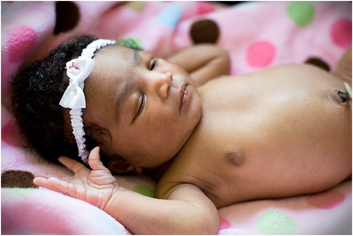 Cerca de la niña recién nacida vistiendo una diadema blanca durmiendo sobre una manta rosa