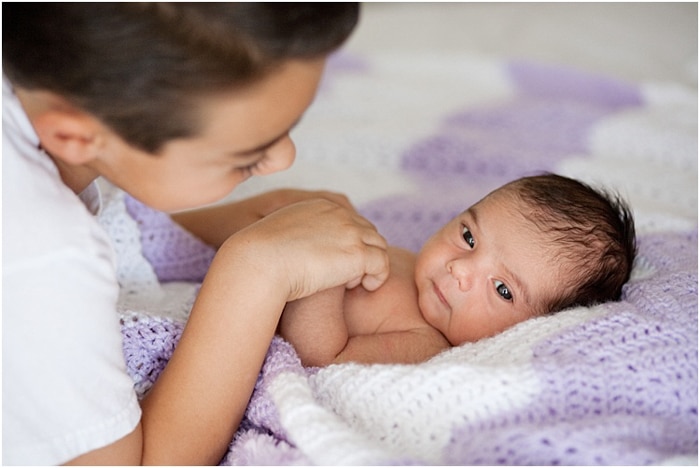 Cerrar hermano mayor sosteniendo las manos del bebé recién nacido durante una sesión de retrato del recién nacido