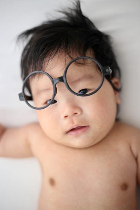Adorable bebé con gafas redondas y cabello negro desordenado