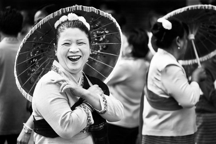 Un retrato callejero en blanco y negro de una mujer con un paraguas riendo con amigos antes del inicio del desfile anual de flores.  Consejos de fotografía narrativa