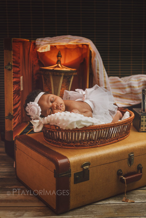 un recién nacido posado en la parte superior de una maleta entre otros accesorios de fotografía de recién nacidos
