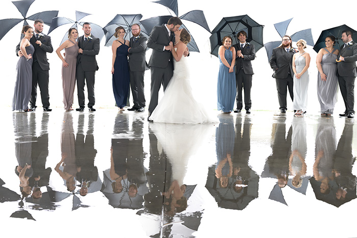 Una foto de boda grupal de la fiesta nupcial sosteniendo paraguas bajo la lluvia.