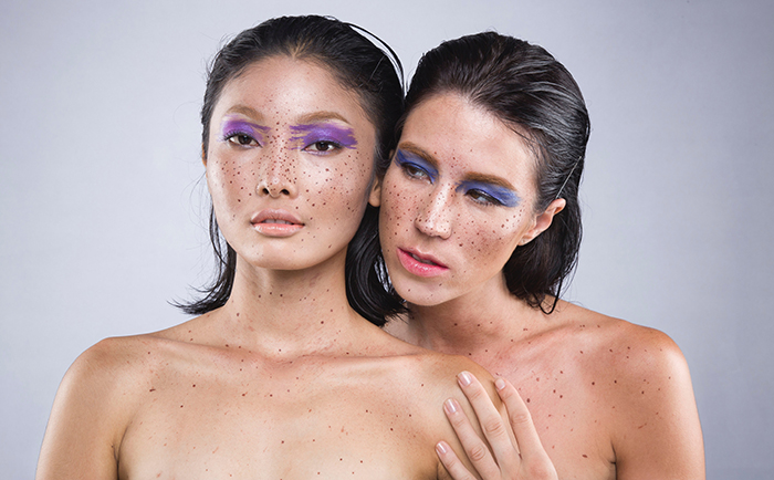 Fotografía de desnudos artísticos de dos modelos femeninas desnudas con delineador de ojos morado y pecas enfatizadas 