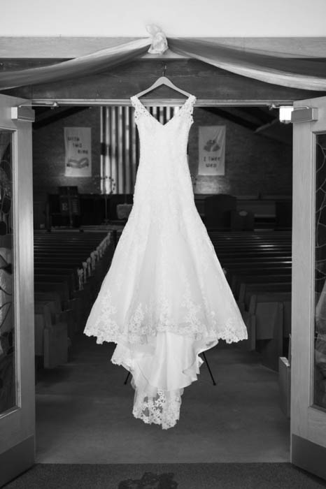 Una foto de boda en blanco y negro de un vestido de novia colgado sobre las puertas de la iglesia