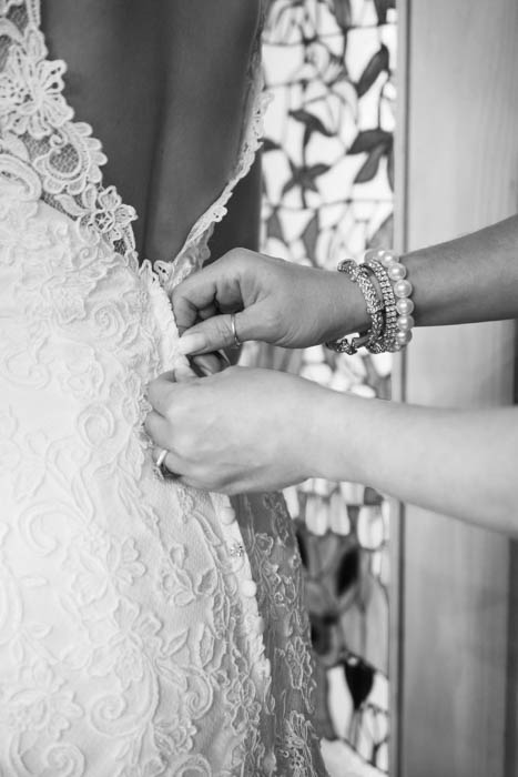 Una foto de boda en blanco y negro de la madre de la novia abrochándose el vestido de novia