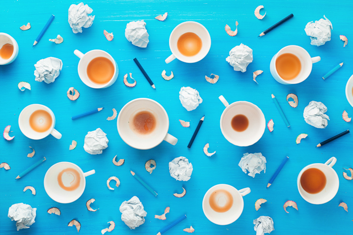 Lugar de trabajo de profesión creativa con tazas de café vacías, bolas de papel arrugadas y virutas de lápiz sobre un fondo azul colorido.  Concepto de inspiración minimalista con esquema de color naranja y azul