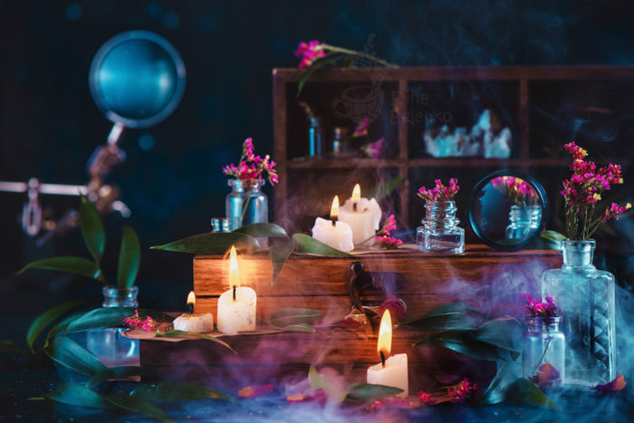 Lugar de trabajo de mago o bruja con velas encendidas, hierbas, cajas de madera antiguas y humo.  Bodegón de fantasía oscura con esquema de color azul y naranja
