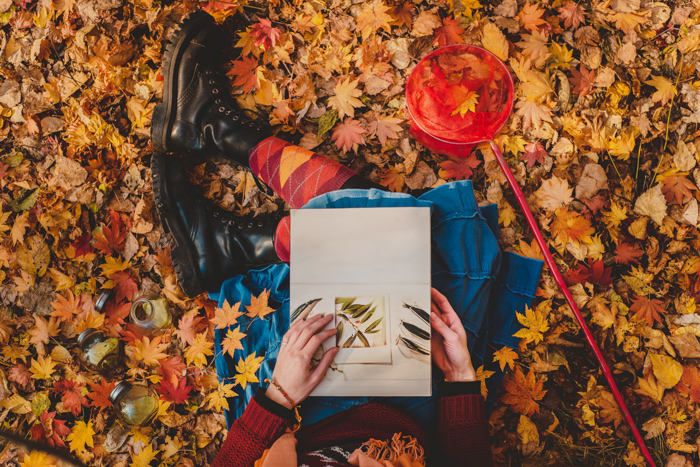 Una imagen cenital de una persona leyendo un libro blanco sentada entre hojas de otoño