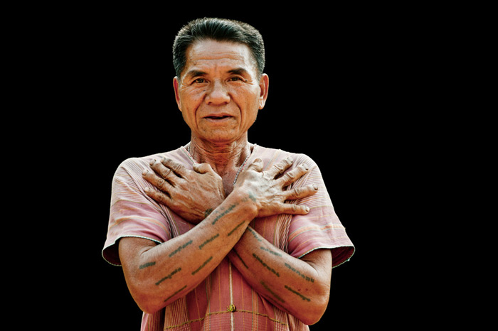 Un hombre de Karen muestra sus tatuajes tradicionales sobre un fondo negro en un estudio de fotografía de retratos al aire libre.