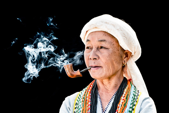 Foto de una mujer tailandesa fumando una pipa contra un fondo negro en un estudio de fotografía de retratos al aire libre.