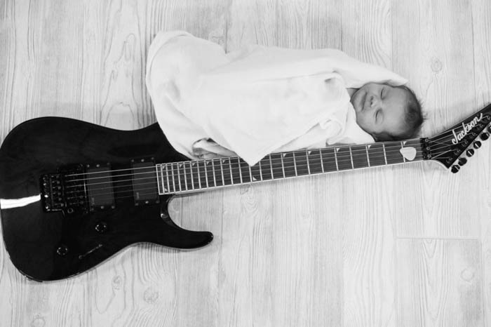 Fotografía en blanco y negro de un recién nacido fotografiado cerca de una guitarra.  poses de fotografía de recién nacido