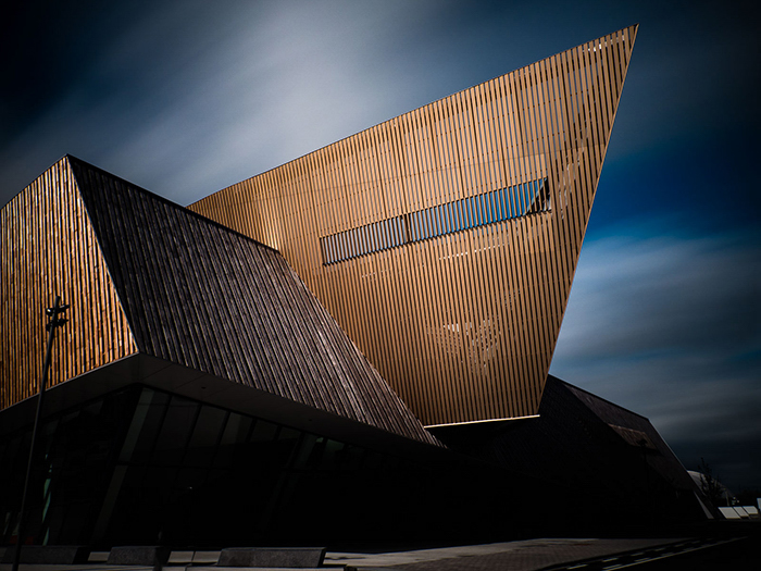 El Palacio de Congresos de Mons (Bélgica).  Estructura geométrica marrón rojiza en contraste con un cielo azul más oscuro