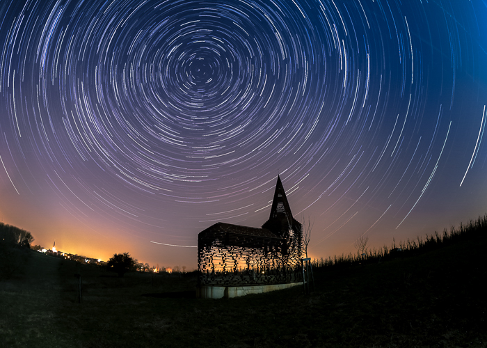 silueta de la Iglesia See Through iluminada cálidamente desde atrás, debajo de un rastro de estrellas y un atardecer azul anaranjado