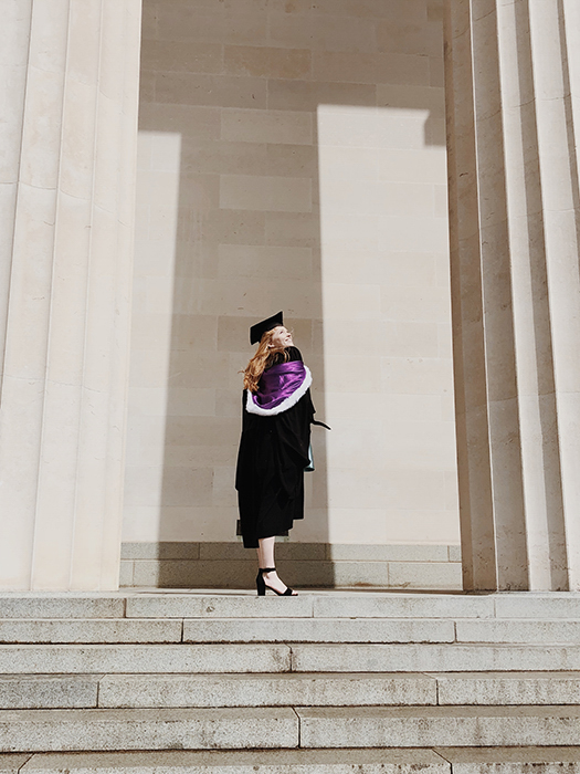 un estudiante con ropa de graduación posando en los escalones