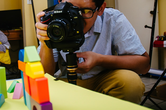 un hombre fotografiando bloques de construcción de juguete con una Nikon DSLR