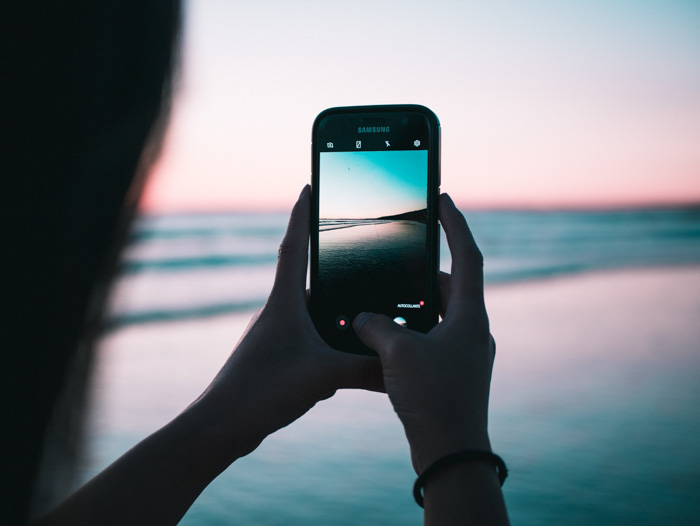 una niña tomando una foto de playa en un teléfono inteligente al atardecer