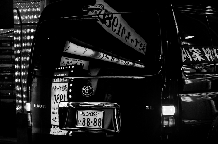 Imagen en blanco y negro de la parte trasera de una camioneta negra con reflejos de los edificios alrededor 