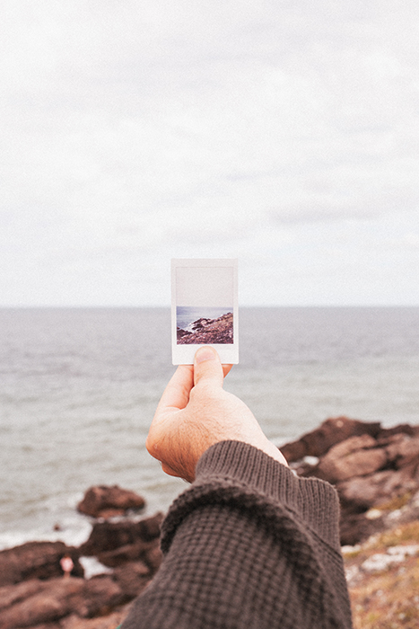 Foto de una mano sosteniendo una foto Polaroid de una playa