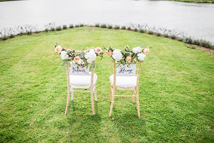 Una foto luminosa y aireada de dos sillas de boda decoradas que se utilizarán como fondos de retratos de boda.