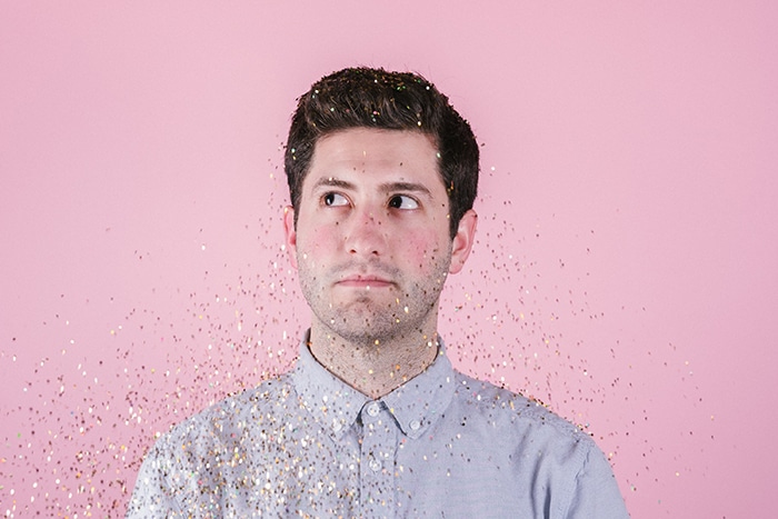 Retrato de un hombre cubierto de brillo que cae posando delante de un fondo de fotografía rosa