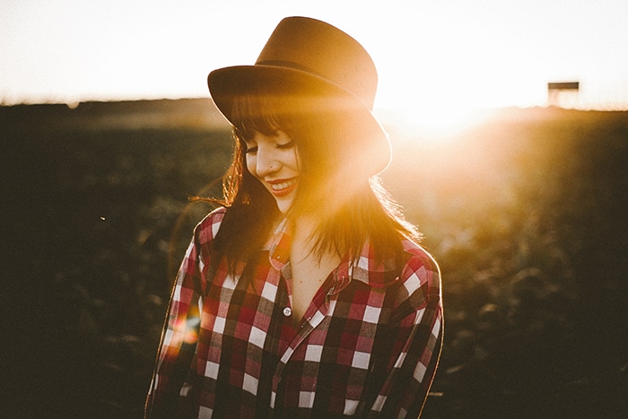 Retrato de una modelo femenina con sombrero con el brillante resplandor del sol detrás de ella sirviendo como un interesante retrato de fondo