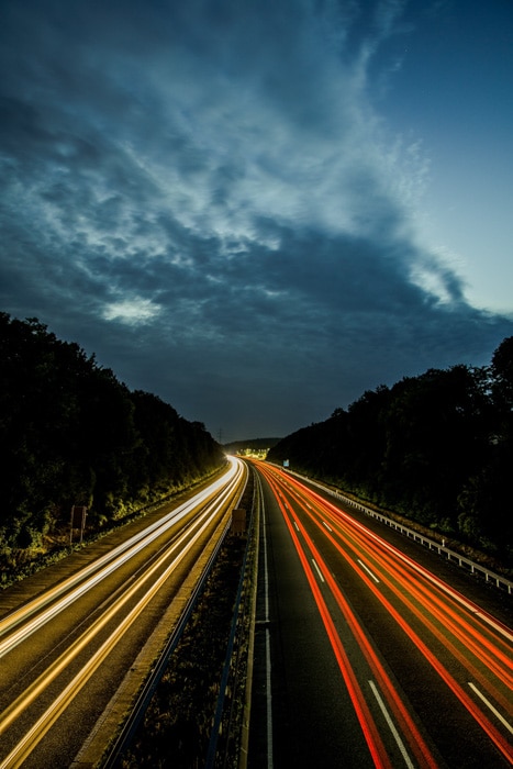 Una vista aérea de una carretera en la noche con corrientes de colores de estelas de luz de automóviles capturadas utilizando las reglas 180 para el desenfoque de movimiento.
