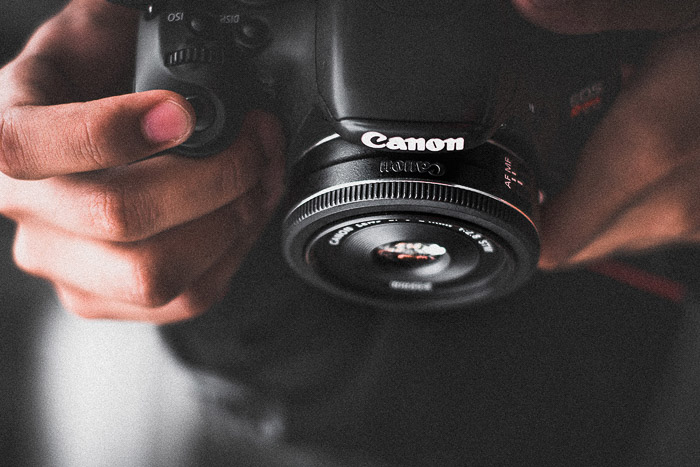 Un primer plano de un fotógrafo sosteniendo una Canon DSLR con lente Pancake
