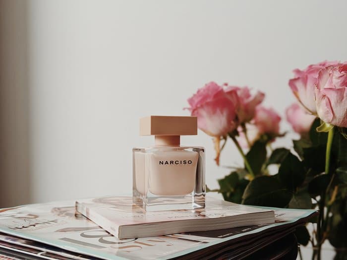 Foto de producto de perfume en un escritorio junto a rosas rosadas