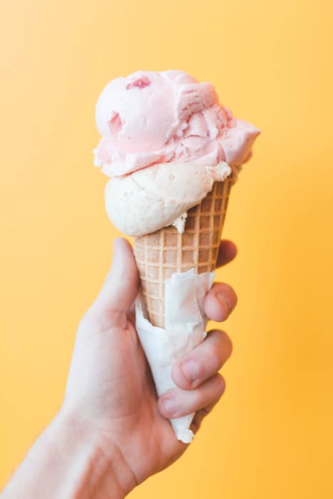 Mano sosteniendo un helado de fresa delante de un fondo amarillo