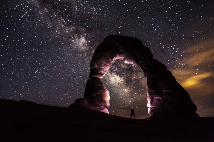 Una impresionante imagen de fotografía nocturna con un hombre bajo un arco de piedra y un cielo estrellado.