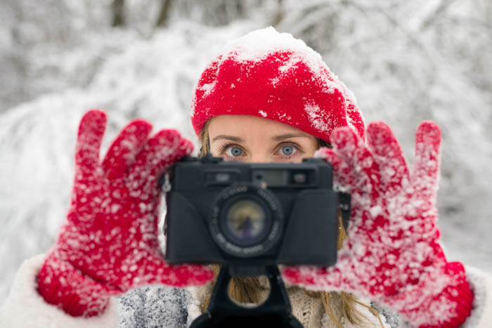 Chica sosteniendo una cámara en sus manos mientras usa guantes de fotografía