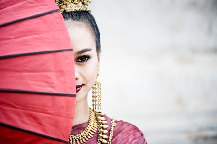 Una hermosa modelo femenina posa detrás de un paraguas rojo - accesorios de fotografía
