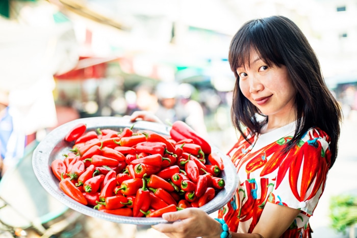 Joven mujer bastante asiática en un mercado al aire libre con chiles.  - accesorios de fotografía